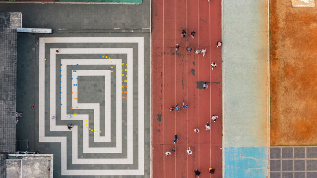 Aerial view of a running track with people exercising next to a paved area featuring a geometric maze pattern in Indonesia.
