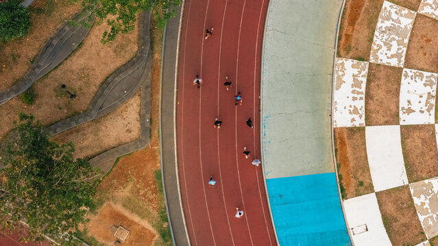 Aerial view of people running on a red athletic track with a blue lane and a checkered pattern area in a park in Indonesia.