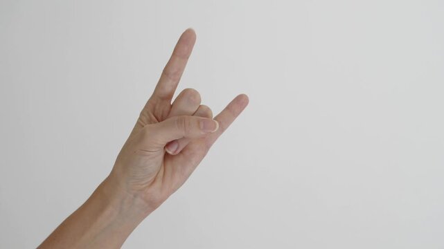A hand repeatedly making the rock and roll horns gesture against a clean white neutral background and negative space create a versatile visual for rock music or concerts