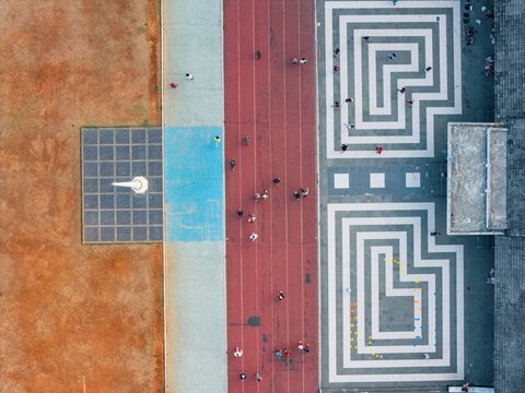 Aerial view of a sports track with people running and walking alongside a patterned paved area and a dirt field in Indonesia.