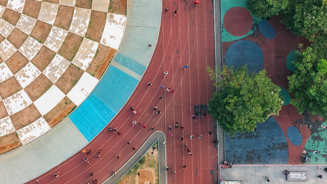 Aerial view of people running and walking on a red athletic track surrounded by a checkered pattern area and green trees in Indonesia.