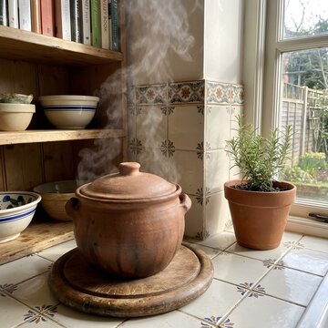 Steaming clay pot on a kitchen trivet in a rustic home kitchen setting