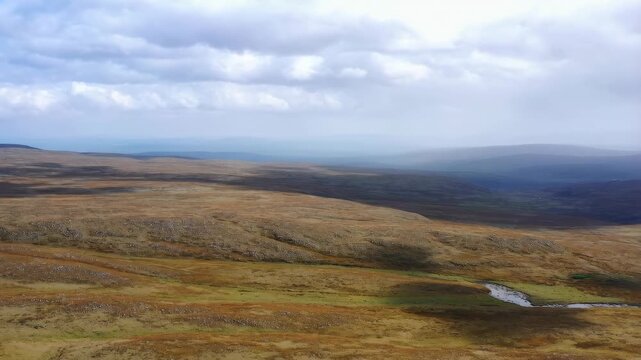 Open moorland landscape with a winding stream beneath cloudy skies and distant rolling hills. Nature documentaries, travel promotion, and wilderness tourism.
