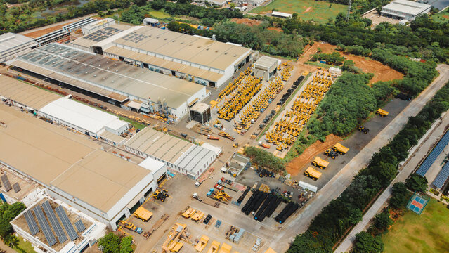 Aerial view of a large cranes manufacturing facility featuring industrial warehouses, rows of yellow construction machinery, and solar panels on rooftops in India.