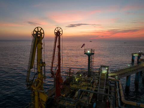 Aerial view of an offshore industrial jetty with large cranes and pipelines extending into the sea during a vibrant sunset in Ratnagiri, Maharashtra, India.
