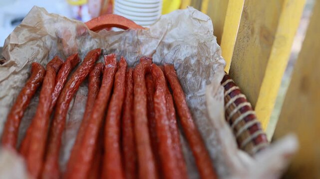 Traditional dried sausages in wicker basket with parchment paper. Smoked thin salami sticks on rustic market stall. Homemade meat snack and street food concept