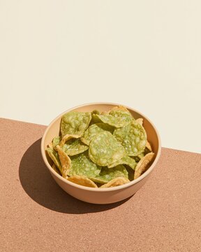 Bowl of green potato chips on a textured brown surface with off-white copy space, perfect for snack advertising and party menus