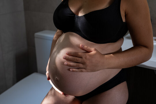 Pregnant woman holding her belly in black lingerie, showing new life