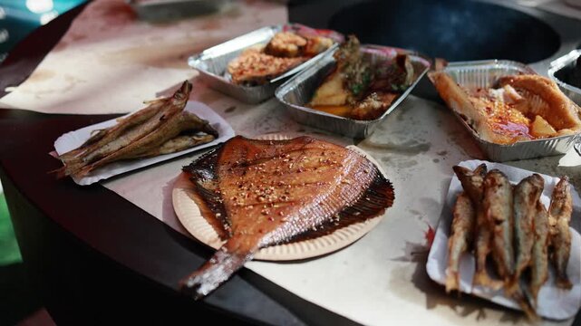 Grilled skate fish with spices served on paper plate at street food market. Fried seafood dishes and smoked fish on table, delicious street cuisine concept