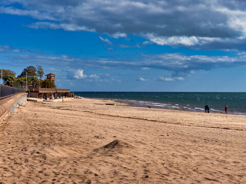 Sunny day at the coastal beach with sandy shore, promenade, and blue sky with white clouds