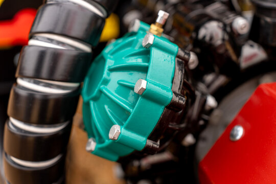 Close-up of turquoise high pressure diaphragm pump with metal bolts installed on agricultural machinery.