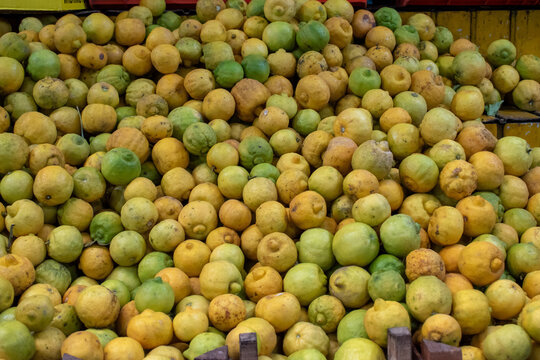 A detailed close-up shot of a large, vibrant pile of freshly picked green and yellow organic limes, ready for sale at a bustling Mayor's Market stall. Ideal for recipes.