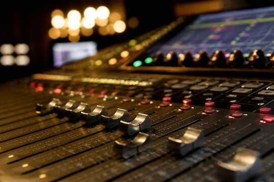 A close-up of a professional audio mixing console with knobs and faders in a dimly lit studio setting.