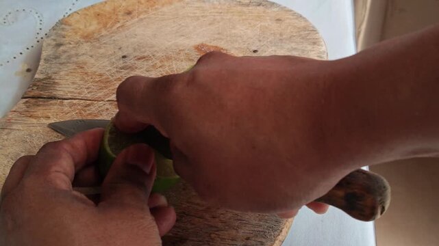 Close up of a knife cutting a fresh green lime on a wooden board