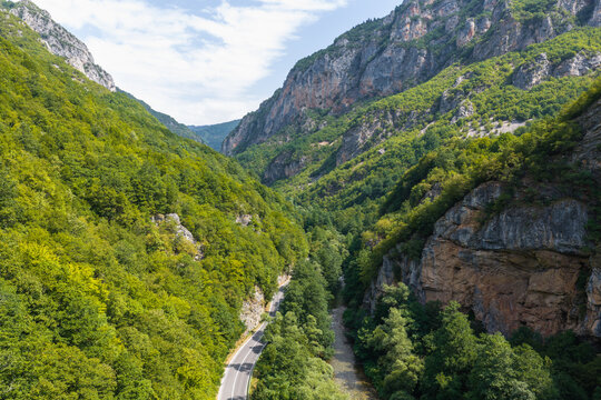 Aerial view of Mavrovo National Park featuring a winding road and a river flowing through a lush green mountain gorge in Mavrove, Municipality of Mavro, North Macedonia.