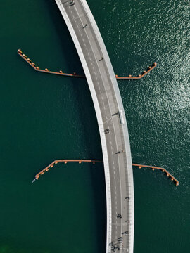 Aerial view of a curved bridge spanning over deep green water with pedestrians walking along the path and wooden piers extending into the sea, Copenhagen, Denmark.
