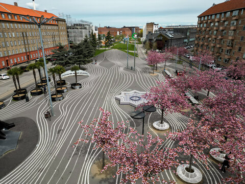 Aerial view of Superkilen Park featuring its iconic black asphalt with white wavy lines, cherry blossom trees in bloom, and modern urban design elements in Copenhagen, Denmark.