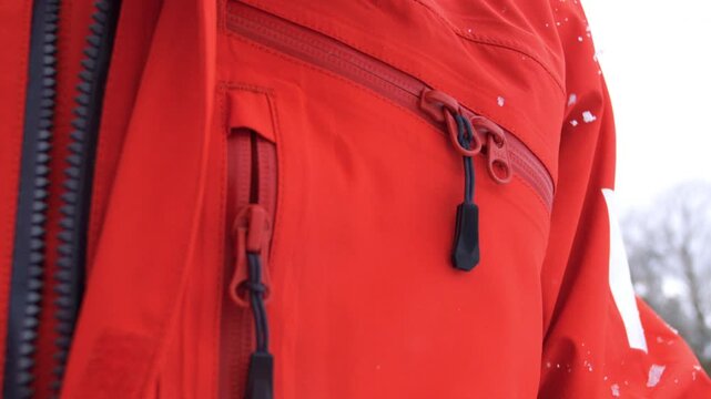 Snow floats around heavy-duty zippers on a red winter jacket in cold outdoor conditions