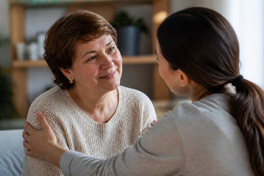 Two women, an older woman and a younger woman, are having an intimate conversation indoors.