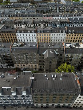 Aerial view of the dense urban landscape of Copenhagen, featuring rows of historic residential buildings with dark tiled rooftops, chimneys, and narrow streets below in Copenhagen, Denmark.