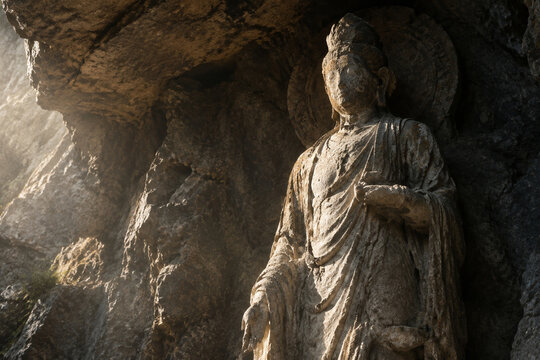 An ancient unfinished stone statue of a deity with a worn face in a rocky alcove.