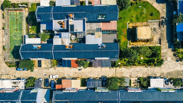 Aerial view of a residential neighborhood featuring blue-roofed houses, a small sports court, and green lawns in Bekasi Barat, West Java, Indonesia.