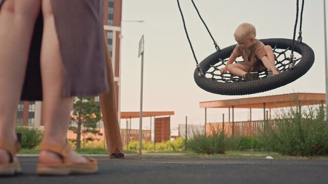 Young boy plays in tire swing at outdoor playground observed by another boy nearby. scene features child interacting with his surroundings and swinging on equipment under natural light set