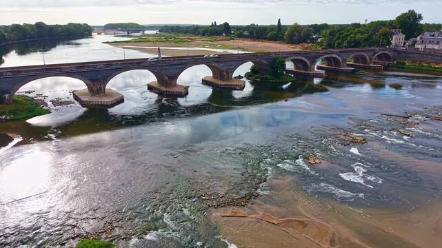 Panning drone fly of Dumnacus Bridge or Pont de Dumnacus spans the shallow Loire River with multiple stone arches and calm flowing water, Maine-et-Loire, France
