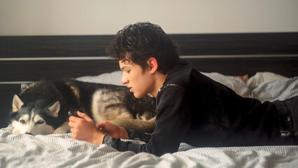 Teenage boy lies on a bed face to face with his Siberian husky and strokes the dog, a warm morning frame about the bond between a teenager and a big northern breed at home © iwavephoto