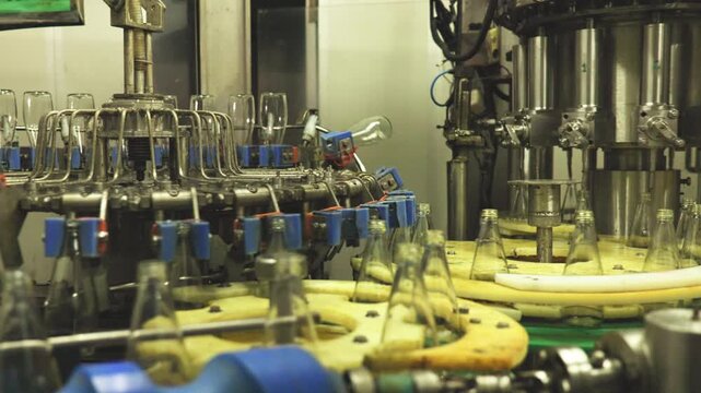 Close-up of industrial bottling equipment precisely filling glass containers with liquid during high-speed beverage production process in factory