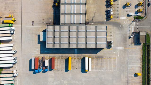 Aerial view of a commercial freight logistics facility with rows of parked semi-trucks and trailers at loading bays in Milan, Lombardy, Italy.