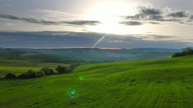 Aerial view of rolling green hills at sunset with soft light and clouds in Tuscany, Italy.