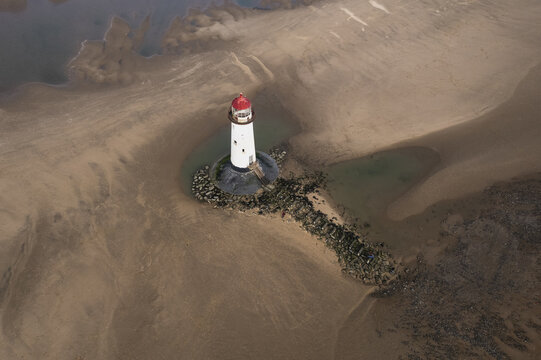 Talacre, Wales, United Kingdom - 25 February 2022: Aerial view of Point of Ayr Lighthouse standing on the sandy beach at low tide with rocky foundations and calm water pools.