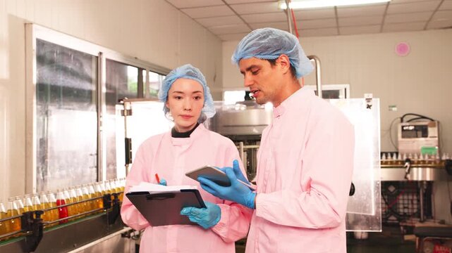 Factory supervisor and worker examining bottled drink against light, assessing clarity and quality during production process in beverage manufacturing facility