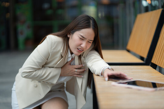 Heart emergency concept. Businesswoman suffers sudden chest pain and reaches for phone while collapsing near a bench. heart, chest, emergency, pain, healthcare
