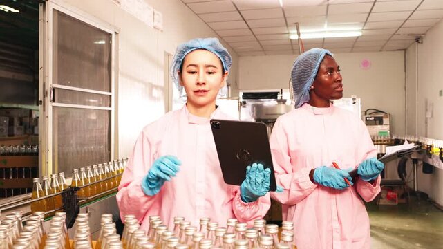 Food factory workers in protective clothing inspecting bottled beverages on production line, recording data for quality control and safety compliance