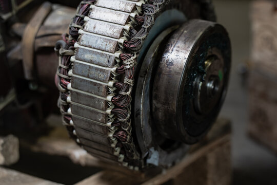 Disassembled electrical machine with exposed copper windings and a laminated metal core beside a circular assembly, representing motor repair and component inspection