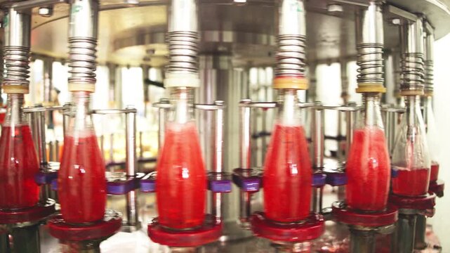Close-up of industrial bottling equipment precisely filling glass containers with liquid during high-speed beverage production process in factory