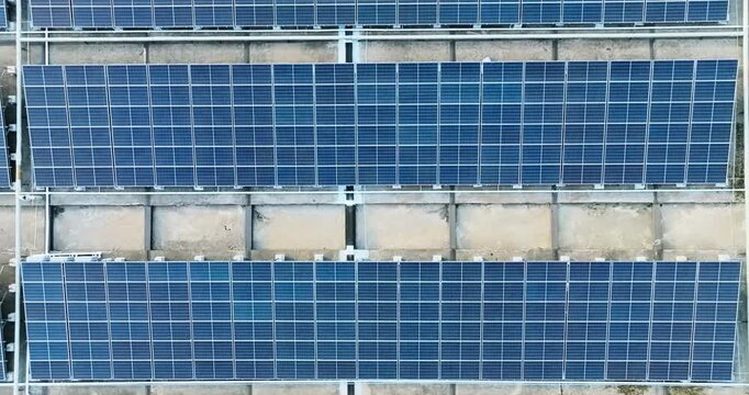 Aerial view of blue solar panels arranged in rows across a weathered concrete rooftop, with metal frames.