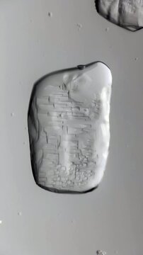 Microscopic footage captures sugar crystal dissolving rapidly inside clear water. Transparent crystal structure erodes quickly while small bubbles float around melting edges completely