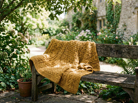 Mustard Yellow Knitted Blanket Draped Over Wooden Garden Bench in Lush Green Garden