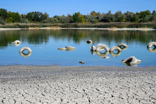 A calm lake reflects the blue sky and surrounding foliage. Abandoned tires are partially submerged, creating an intriguing pattern.