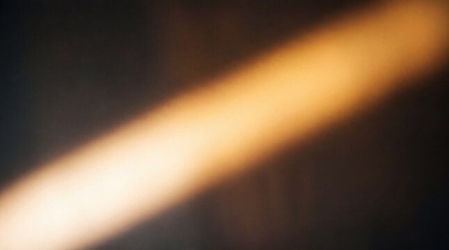 A warm golden diagonal light beam shining through a dark and moody atmospheric space
