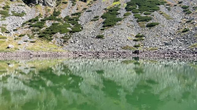 Panning shot of the emerald glacial Lake Mija and rocky alpine slope in Parang Mountains, Romania. Nature and travel video, 4K, 60fps.