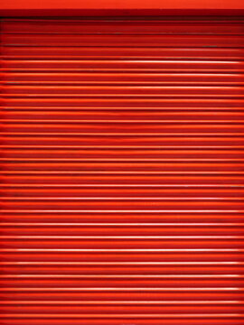 Red shutter door with horizontal pattern and strong color impact. Front view with clear geometry and urban context. Copy space.