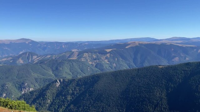 Wide panoramic view of vast mountain ranges, green forests, and ridges under a clear blue sky in Parang Mountains, Romania. Nature and travel video, 4K, 60fps.
