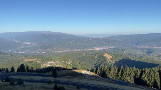 Panning shot of a winding mountain road, green valleys, and localities in Jiului Valley visible from Parang Mountains, Romania. Nature and travel video, 4K, 60fps.