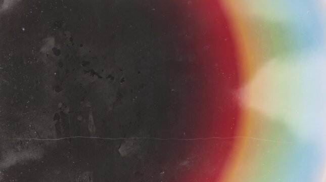 Vintage texture with dust, scratches, and a bright rainbow light leak on dark black background
