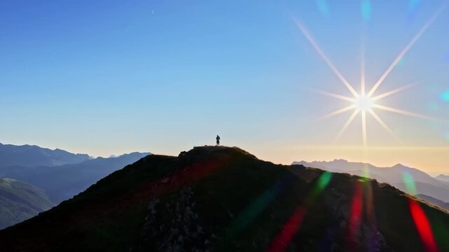 A small hiker silhouette reaches the crest of a dark mountain ridge beneath a brilliant sunburst