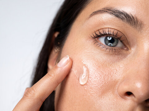Woman applying skincare serum gel to her face, close up shot of glowing skin and cosmetics